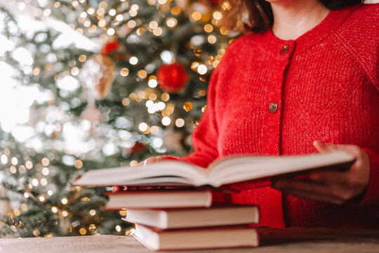 Woman reading an open book near a glowing Christmas tree. winter vacation articles, literacy campaigns,bookstore promotions,home education and cozy festive lifestyle designs 