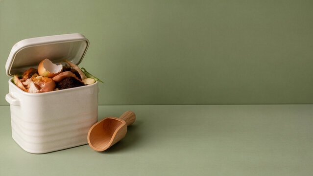 Kitchen Compost Caddy With Food Scraps on Green Background