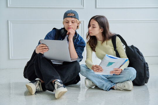 Two focused teenage students looking at laptop screen while studying together on floor