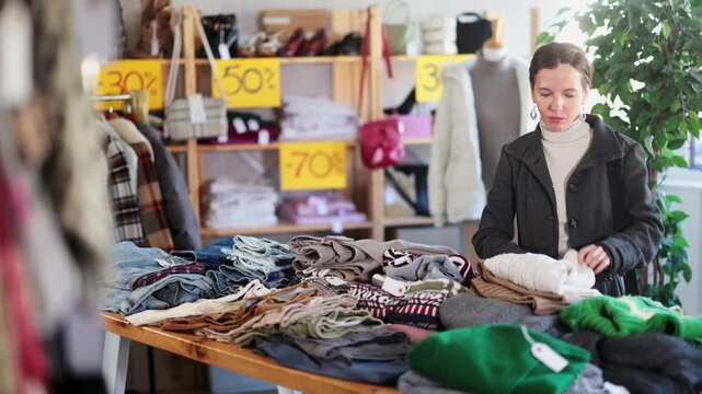 Attentive middle-aged woman looking for warm pullower while shopping in retail outlet 