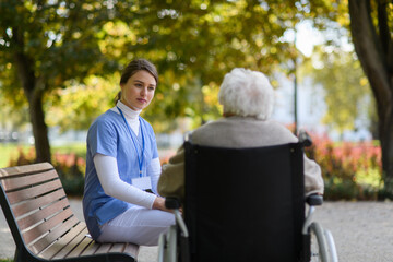 Disabled elderly woman in wheelchair holding hands with her nurse, talking about her problems.