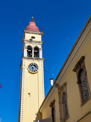 Fototapeta premium Yellow church clock tower with red dome and arched windows under blue sky in Corfu, Greece