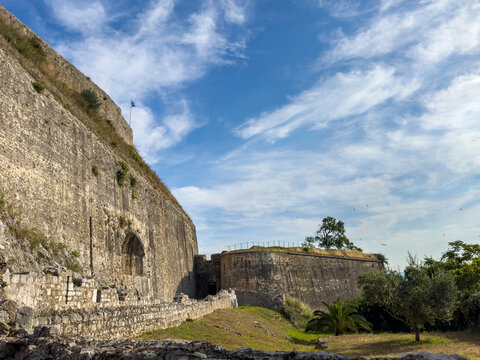 New Fortress weathered stone ramparts above grassy paths in Corfu Town, Greece under blue sky