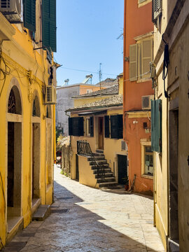 Colorful traditional buildings with shutters on sunny stone alley in Corfu Old Town, Greece