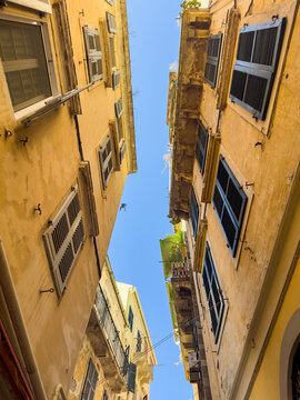 Narrow alley upward view with ochre facades in Corfu old town, Greece
