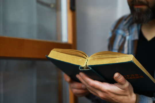 Man Reading an Old Book Indoors Near a Wooden Door for Relaxation and Knowledge