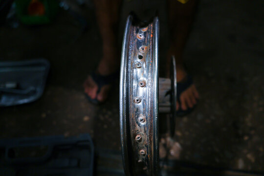 Bicycle wheel rim repair drilled metal mechanic hand outdoors low light workshop close up of worn alloy part with hole pattern and blurred worker foot