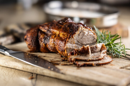 Tasty roasted pork neck with a crispy crust is garnished with fresh rosemary and sliced on a wooden board.