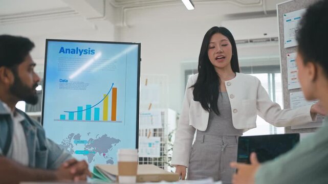 Businesswoman presenting financial charts to colleagues in modern office meeting.