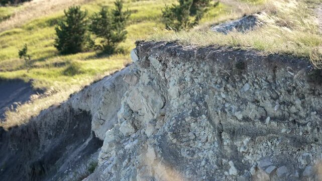 Small pieces of rock and soil crumbling down a steep, grassy cliff face during a landslide, showcasing the natural process of erosion on a sunny day with gentle wind blowing