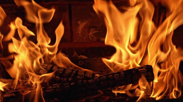 Bright orange tongues of fire flicker and swirl around smoldering wood logs inside a cozy brick fireplace during a tranquil night of warmth and relaxation.