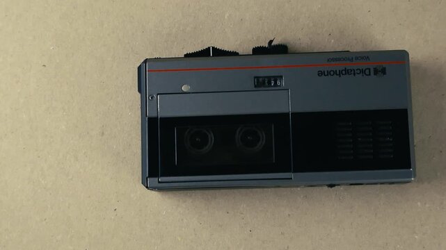 Close up top view of a retro dictation machine with a rolling microcassette tape inside. The old portable device records or plays back sound, representing outdated technology and spying