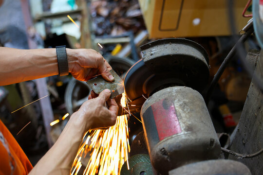 Metalworker, grinding machine, sharpen, tool, spark, workshop hands, abrasive wheel cutting metal with bright orange spark in industrial repair workspace