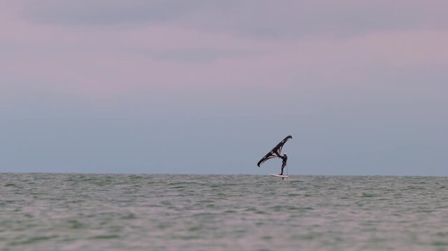 An athlete standing on the board holds on to the wing, in which the wind creates thrust in slow motion. Wingfoil board where a surfer glides through the water on a hydrofoil board..