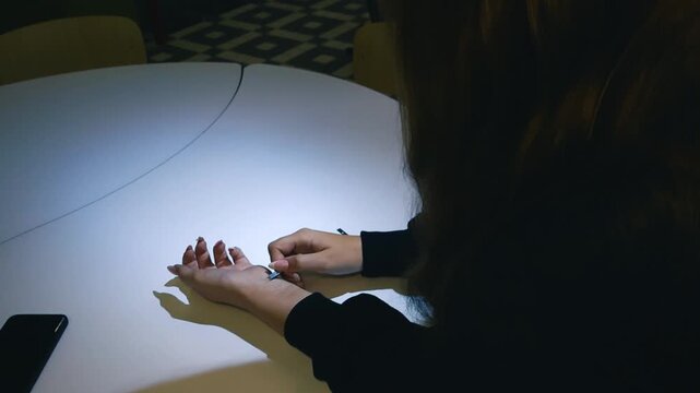 Young woman sitting at a table in a dark room inserting a small RFID chip under the skin of her hand for biohacking, identification, and contactless payment in a futuristic concept