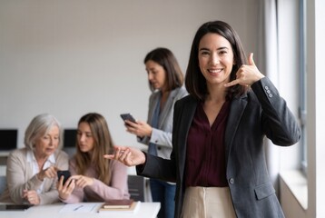 Fototapeta premium Confident businesswoman inviting contact with a gesture while colleagues use smartphones in the background