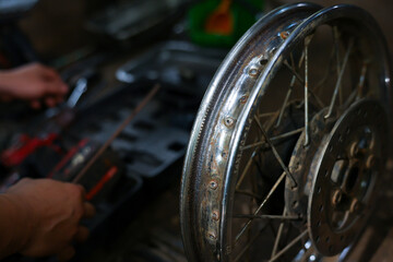 Fototapeta premium Motorcycle wheel repair dim workshop mechanic hands tool close up showing spoke rim maintenance with blurred workbench, gritty garage setting, focused manual labor