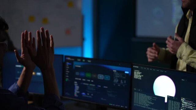 A composed presenter holding a tablet waits out a question with both hands on the device while the wall display keeps running inside a dimly lit machine learning startup office.