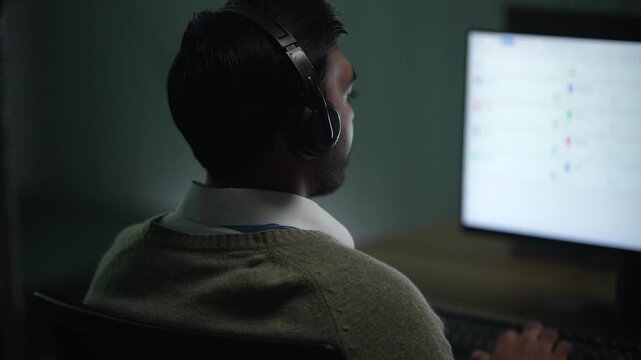 Dual displays seen past a developer's shoulder carry a node graph and an execution panel while his hands stay resting on the keyboard inside a dark AI startup office.