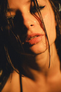 Cinematic, grainy close-up portrait of a young woman with wet skin and hair under dramatic moody lighting. Edgy alternative fashion and emotional concept.