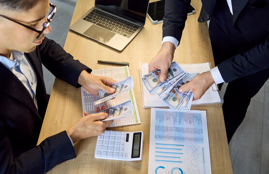 Managers counting cash salary for payroll payment. Two colleagues at office desk verify wages in dollars with calculator and documents, checking finance reports. Clear concept of payroll control.
