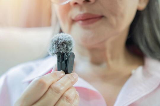 Close-up of an older woman holding a mini wireless lavalier microphone with a furry windscreen