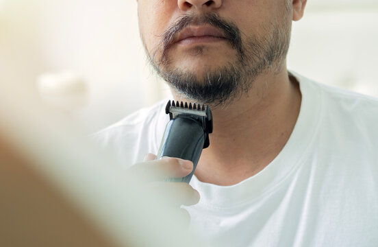 Cropped shot of man using an electric beard trimmer under his chin and jawline.