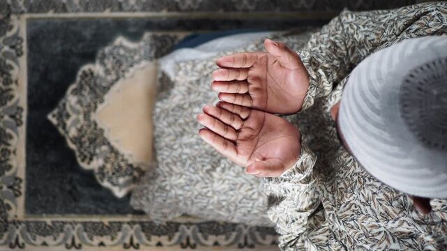 A muslim man prays with hands held open. The setting is simple and focuses on faith