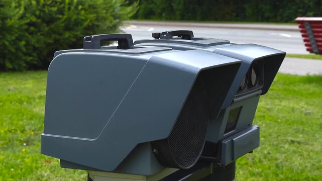 Modern police lidar speed camera gun standing on a tripod by the roadside for traffic monitoring and speed limit enforcement, measuring the velocity of passing vehicles in an urban area