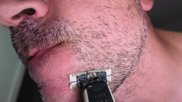Extreme close-up of a man trimming his beard stubble with an electric trimmer