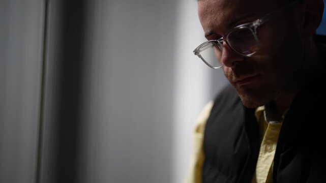 A focused engineer holding a whiteboard marker writes directly on the glass planning wall while the team works on in the darkness behind him in a dark tech office.