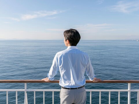 クルーズ船のデッキから遮るもののない青い海と空を眺める男性の後ろ姿