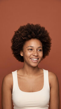 Playful young woman with afro hair laughing on terracotta background