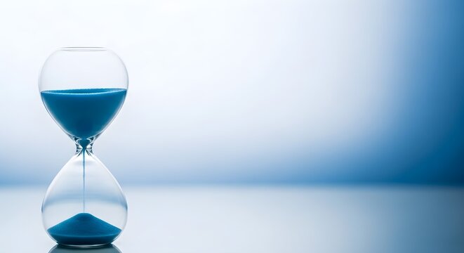 Hourglass with blue sand on a clean reflective surface. Classic sandglass timer showing running out of time. Conceptual studio photography for deadline, patience, and time management.