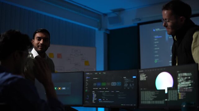 A speaker in a dark knit sweater presents an AI agent architecture to a seated audience, the huge screen behind him full of live metrics inside a dark AI startup office.