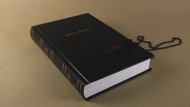 Dramatic close up of a wooden crucifix necklace landing and bouncing on the black leather cover of the Holy Bible, symbolizing faith, devotion, spirituality, and religious belief