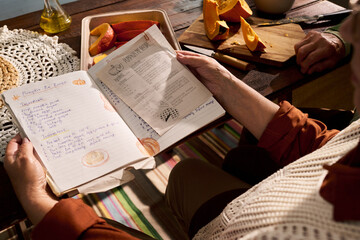 Senior Caucasian woman reading handwritten pumpkin pie recipe book while preparing autumn meal....