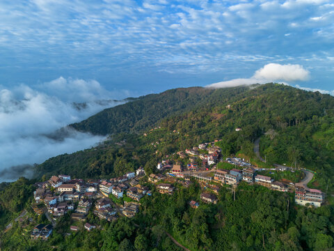 Thailand mountain village landscape misty forest ridge with scattered home beneath textured blue sky, calm rural hill settlement among cloud, road, tree, and valley