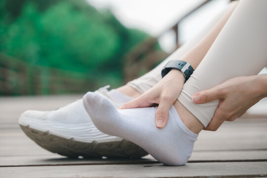 Runner woman experiencing ankle injury pain, seeking rest on floor for physical pressure relief from joint inflammation after fitness running exercise, holding injured foot