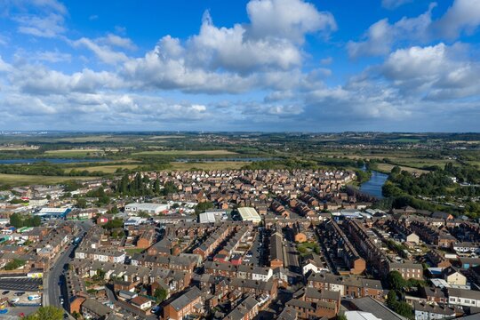Wide aerial view across Castleford in Yorkshire showing dense residential streets industrial buildings green countryside and waterways extending beyond the town beneath a cloud filled sky