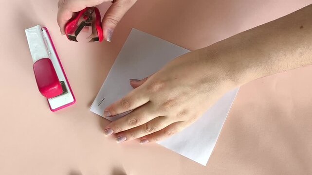 Woman using a staple remover to remove staples from a stack of paper documents on an office desk, representing paperwork, document processing and office work.