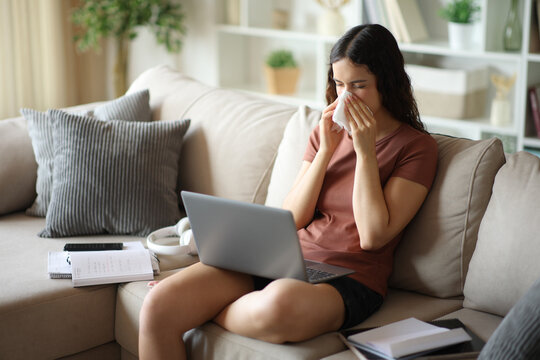 Student with a cold blowing on tissue at studying home