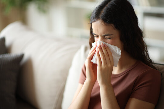 Woman with a cold blowing on paper tissue at home