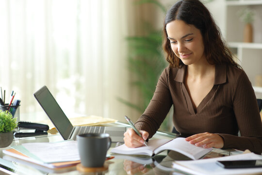 Telecommuter working online at home writing in paper agenda