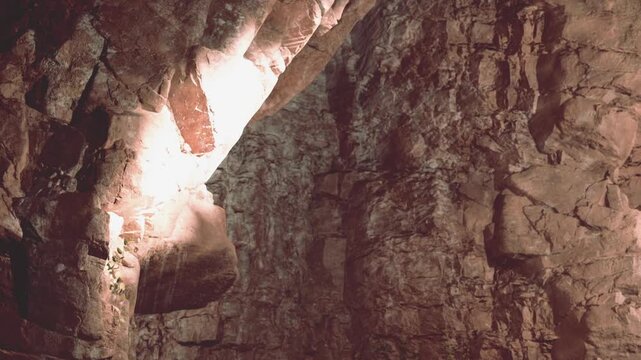 Natural rock formations are visible inside a cave. Light enters through openings in the ceiling, creating shadows on the stone walls. The cave is large and displays layers of rock.
