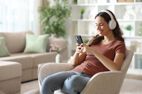 Happy woman on armchair listening music from phone
