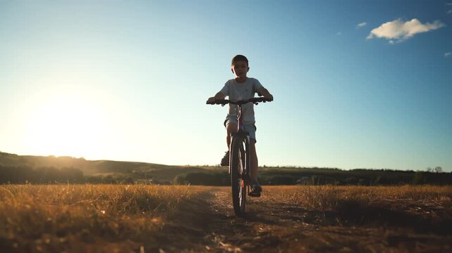 Little boy riding bike in countryside, frontal view in rural landscape in summer . Beautiful scenery in nature, happy kid enjoying freedom and dreaming about traveling, summertime in country, vacation