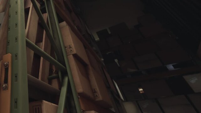 Workers organize and sort many cardboard boxes inside a storage facility. The boxes are stacked against shelves reaching the ceiling. Light comes from above.
