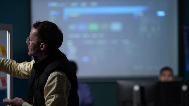 A product lead in profile at the board pauses with the marker at his lips, working out how the two halves of the flow connect inside a dimly lit machine learning startup office.