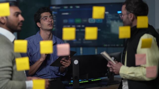 A developer mid explanation at the board takes a red marker passed to him by a teammate without breaking his train of thought inside a dimly lit machine learning startup office.